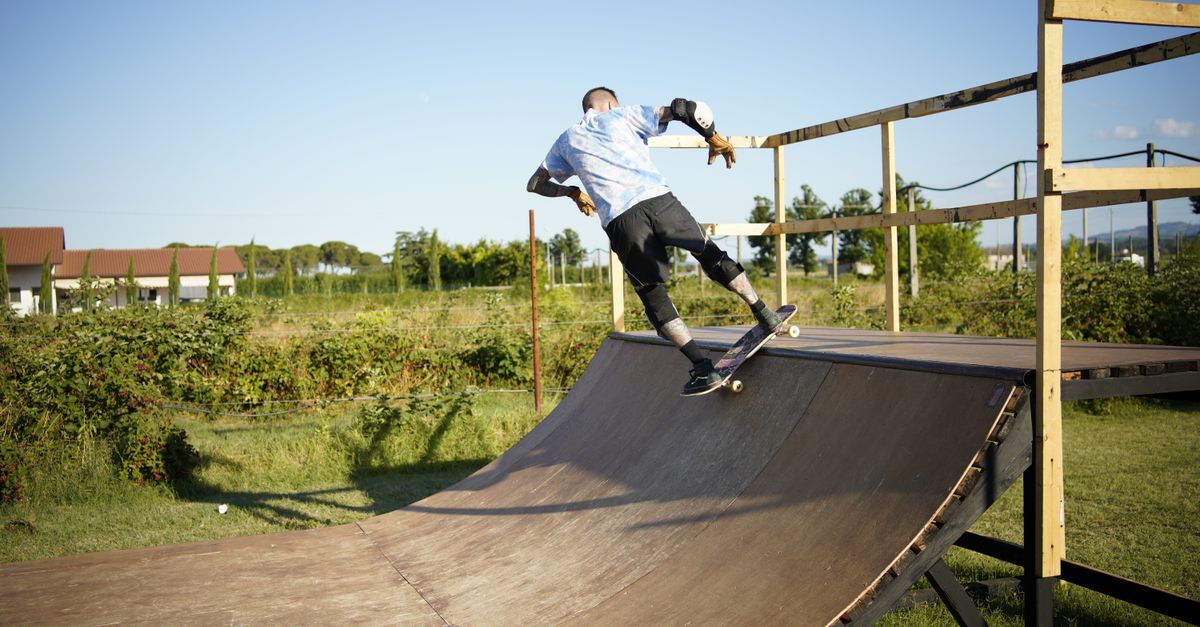 Skateboarder executing a trick on a wooden outdoor skate ramp with lush greenery in the background.